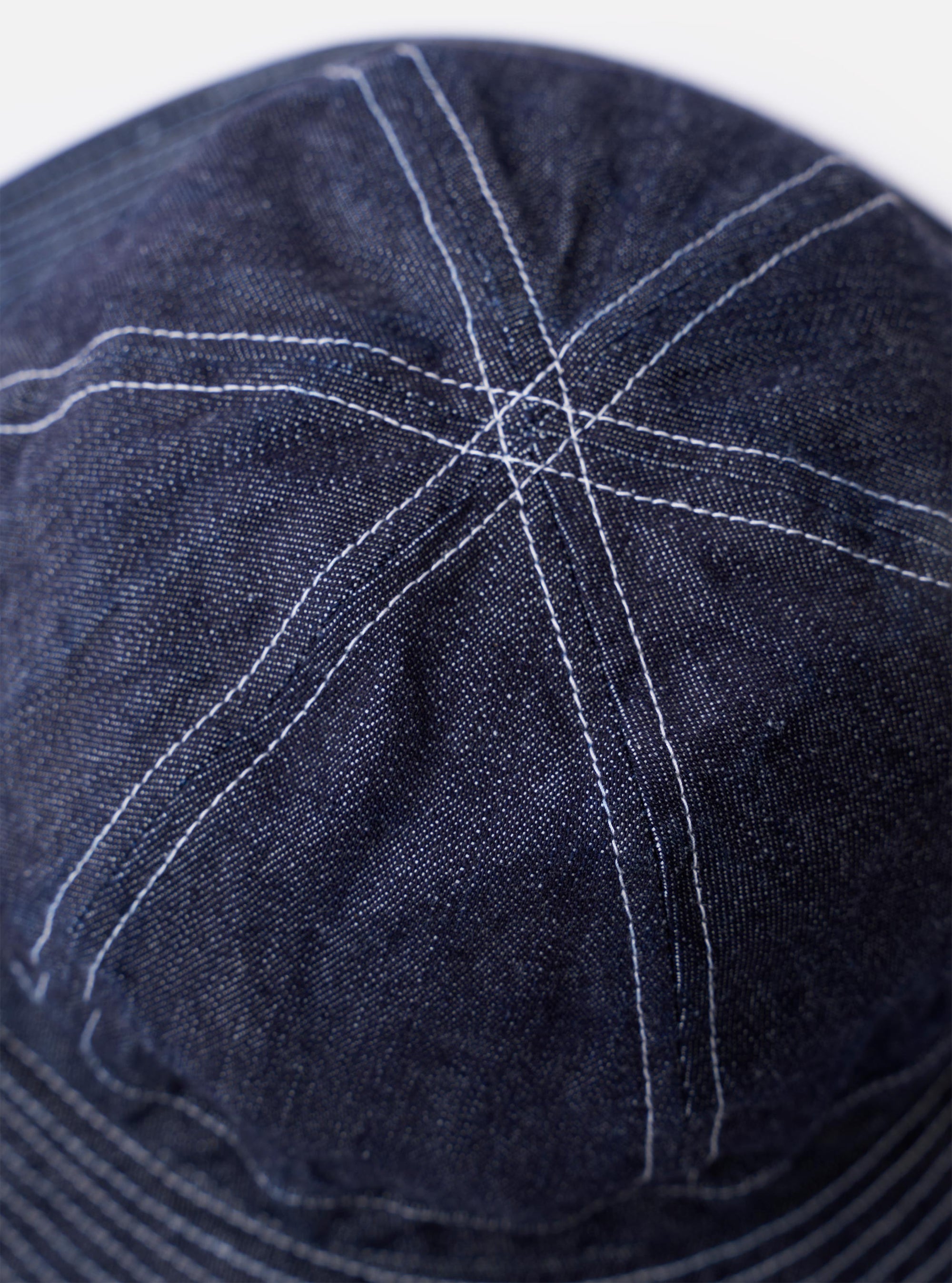 The cableami Indigo 10oz Denim Metro Hat is shown from a rear three-quarter angle as a flat lay against a plain white background. The image highlights the hat's rounded crown, downward-sloping brim, and the adjustable drawstring at the back. The indigo denim fabric features a visible slub texture and tonal stitching.