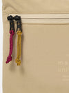 The master-piece x Universal Works Beige Canvas Sacoche is shown from a rear angle as a flat lay against a plain white background. The image highlights the adjustable and removable black crossbody strap attached with metal clips, the clean construction of the back panel, and the durable beige canvas fabric.