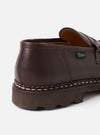 Close-up of the heel and counter of a dark brown leather loafer against a light grey studio backdrop. Visible details include a tan leather lining, a green Paraboot woven label on the heel counter, prominent cream Norwegian welt stitching, and a chunky dark brown rubber lug sole.