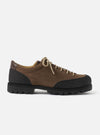 Paraboot Vel low-top shoe in marron suede, shot in profile against a plain light grey studio backdrop. The upper combines brown suede with black textured rubber rand wrapping the toe and heel. A dark brown leather heel counter is visible at the collar. Beige paracord laces thread through five eyelet pairs. The chunky black lug sole has deep zigzag treads.