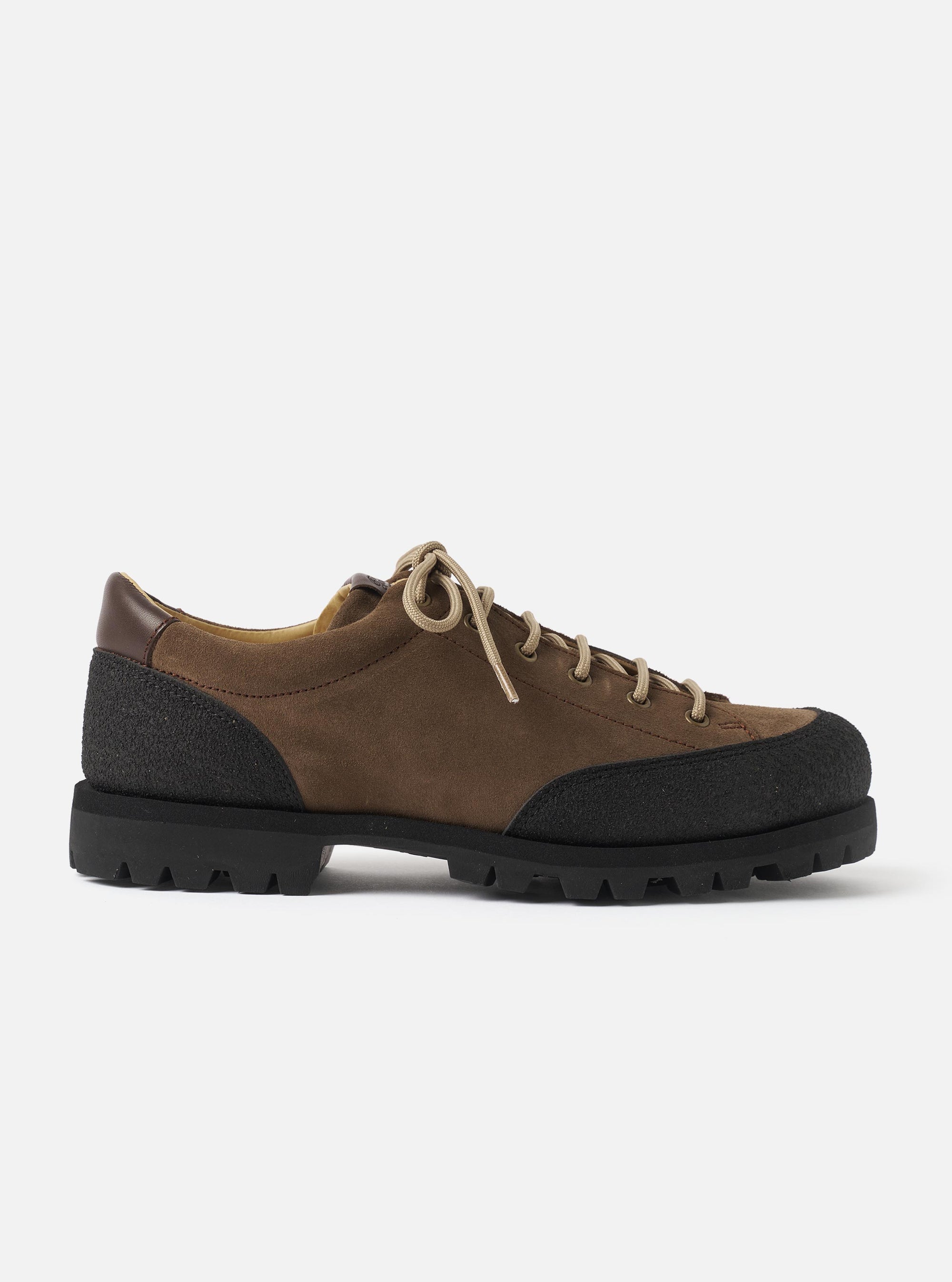Paraboot Vel low-top shoe in marron suede, shot in profile against a plain light grey studio backdrop. The upper combines brown suede with black textured rubber rand wrapping the toe and heel. A dark brown leather heel counter is visible at the collar. Beige paracord laces thread through five eyelet pairs. The chunky black lug sole has deep zigzag treads.