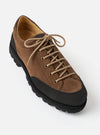 Paraboot Vel Marron suede shoe shot at an angle on a light grey studio backdrop. The tan-brown suede upper features a dark rubber toe bumper, brass eyelets, and beige round laces tied at the top. A dark brown leather collar trim surrounds the tan leather lining. The chunky black lug sole is prominently visible.