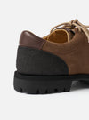 Close-up of the heel and quarter of the Paraboot Vel Marron suede shoe against a light grey studio backdrop. The upper is tan suede with a darker brown smooth leather heel counter and visible stitching. A chunky black lug sole with deep cleated tread is prominent. Beige cord laces and a mustard yellow sock lining are visible at the collar.