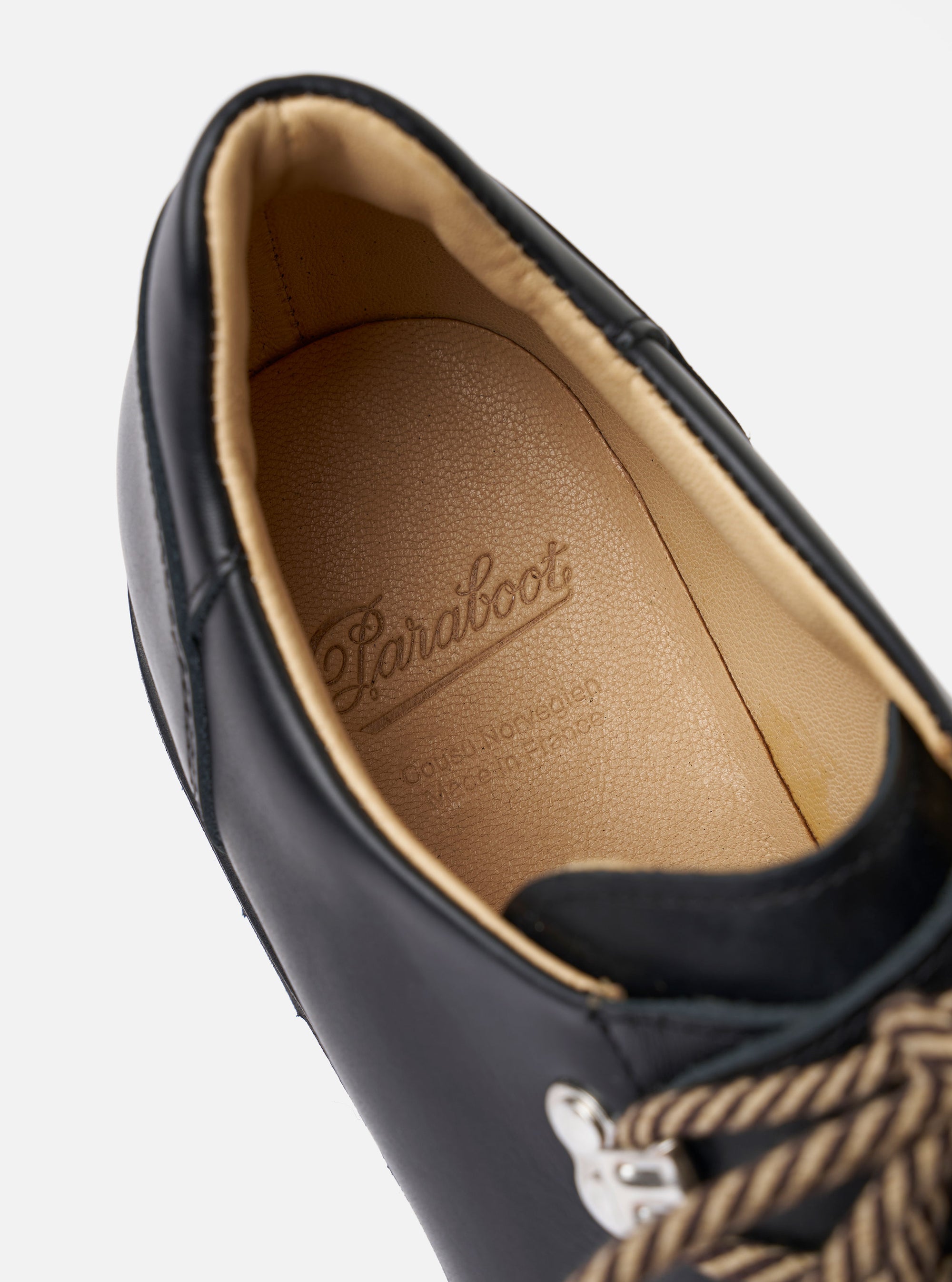 The Paraboot Black Leather Clusaz Jannu is shown from a rear three-quarter angle as a flat lay against a plain white background. The image highlights the low-top silhouette, the sturdy natural rubber lug sole, and the smooth black leather upper. The reinforced heel counter and Norwegian welt stitching are prominent features.
