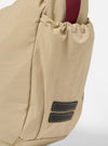 The master-piece x Universal Works Beige Large Canvas Shoulder Bag is shown from the back as a flat lay against a plain white background. The image highlights the adjustable shoulder strap with metal hardware, a small logo patch, and the durable beige canvas fabric.
