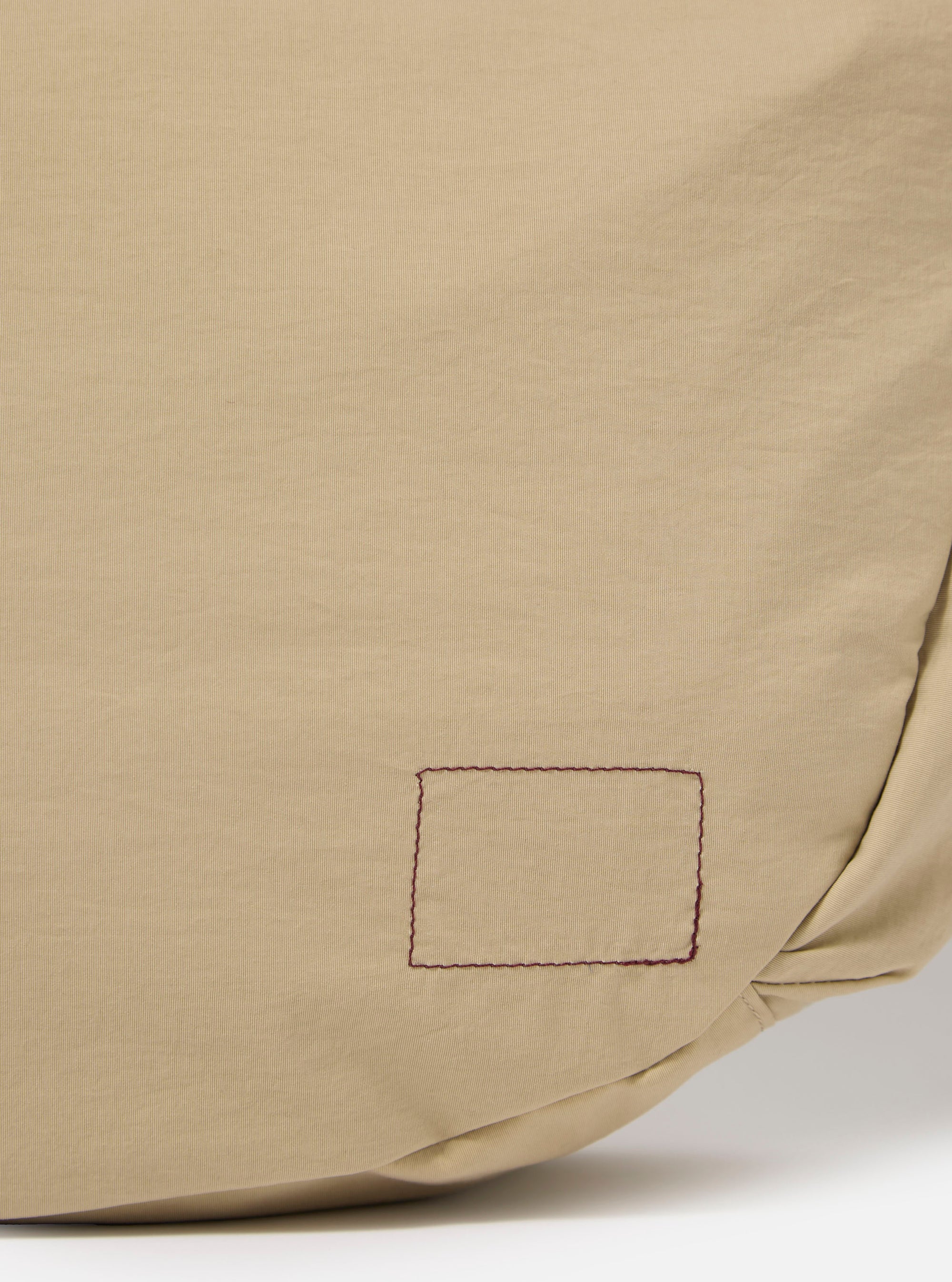 The master-piece x Universal Works Beige Large Canvas Shoulder Bag is shown from the back as a flat lay against a plain white background. The image highlights the adjustable webbed shoulder strap and the clean, rectangular construction of the bag's rear panel in a sand-colored beige fabric.