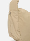 The master-piece x Universal Works Beige Large Canvas Shoulder Bag is shown from a side angle as a flat lay against a plain white background. The image highlights the depth of the bag, the sturdy canvas construction, and the adjustable shoulder strap. A small collaborative logo patch is visible on the side.