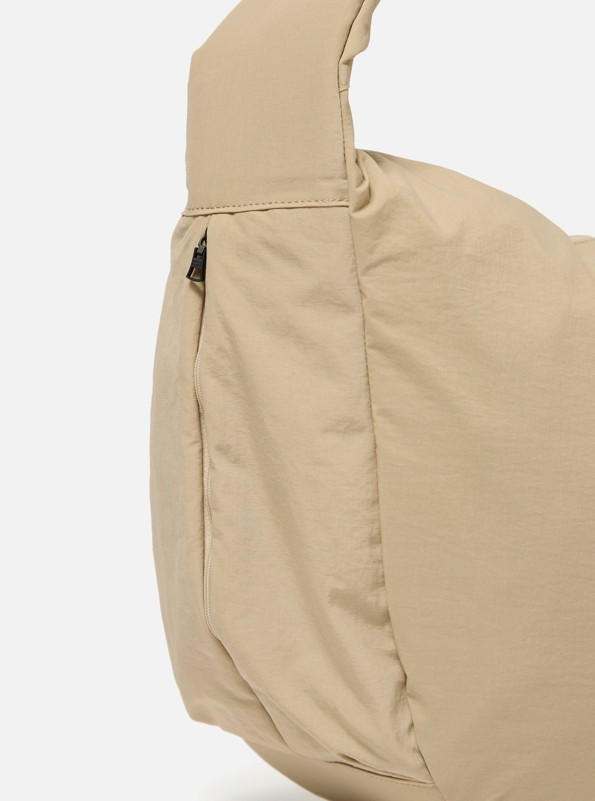 The master-piece x Universal Works Beige Large Canvas Shoulder Bag is shown from a side angle as a flat lay against a plain white background. The image highlights the depth of the bag, the sturdy canvas construction, and the adjustable shoulder strap. A small collaborative logo patch is visible on the side.