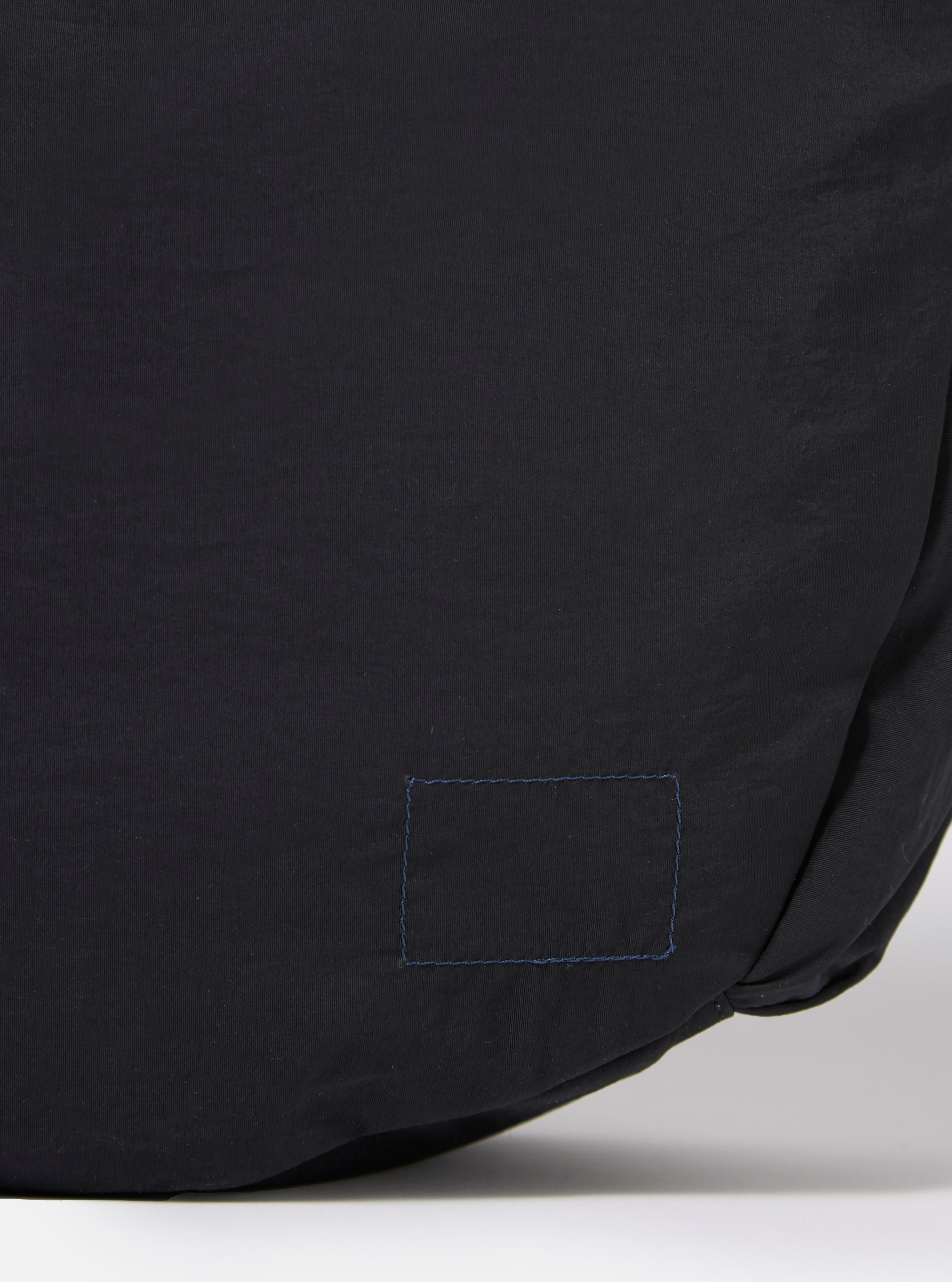 The master-piece x Universal Works Black Large Canvas Shoulder Bag is shown from the back as a flat lay against a plain white background. The image highlights the bag's large, rectangular shape and the textured black canvas material. A horizontal strap is attached across the middle of the back panel.
