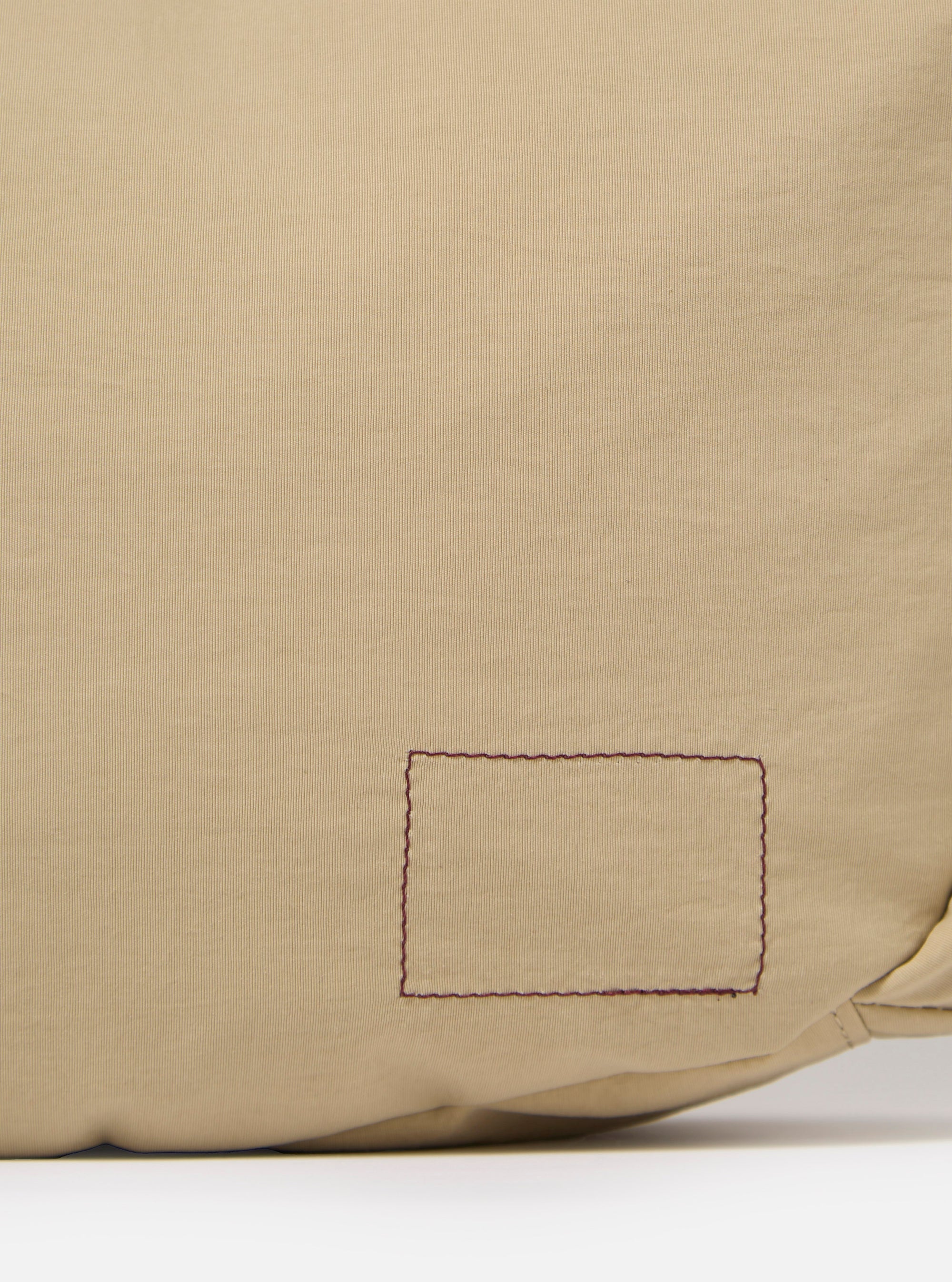 The master-piece x Universal Works Beige Medium Canvas Shoulder Bag is shown from a rear three-quarter angle as a flat lay against a plain white background. The image highlights the adjustable shoulder strap with its black plastic buckle and the clean, structured back panel of the beige canvas bag.