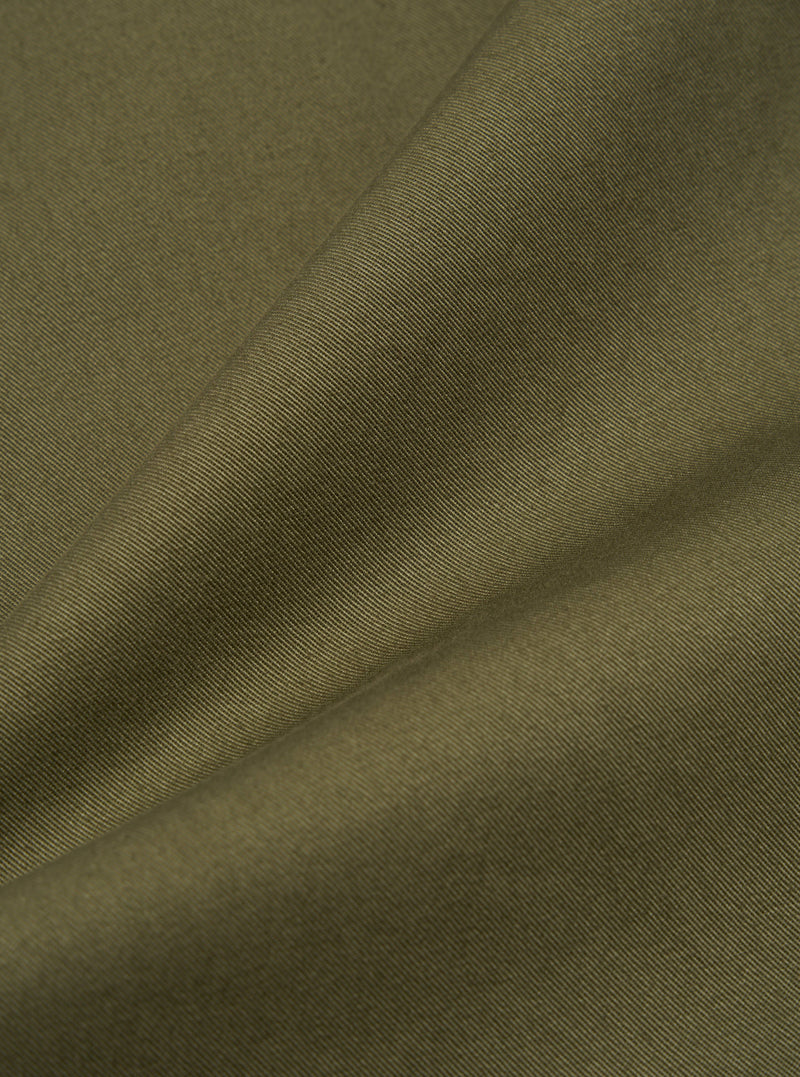 Close-up of the Light Olive Twill Duke Pant fabric. The twill weave is visible, showing the texture and color of the material. The fabric is draped to highlight its quality.