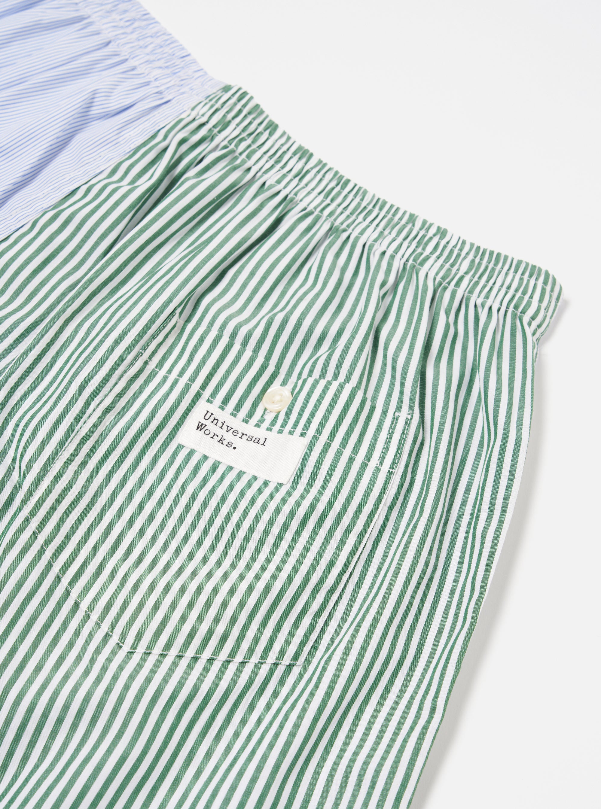 Close-up of the Blue Classic Mix Boxer Short on a white surface. Features green and white stripes, a pocket with a button, and the Universal Works logo.