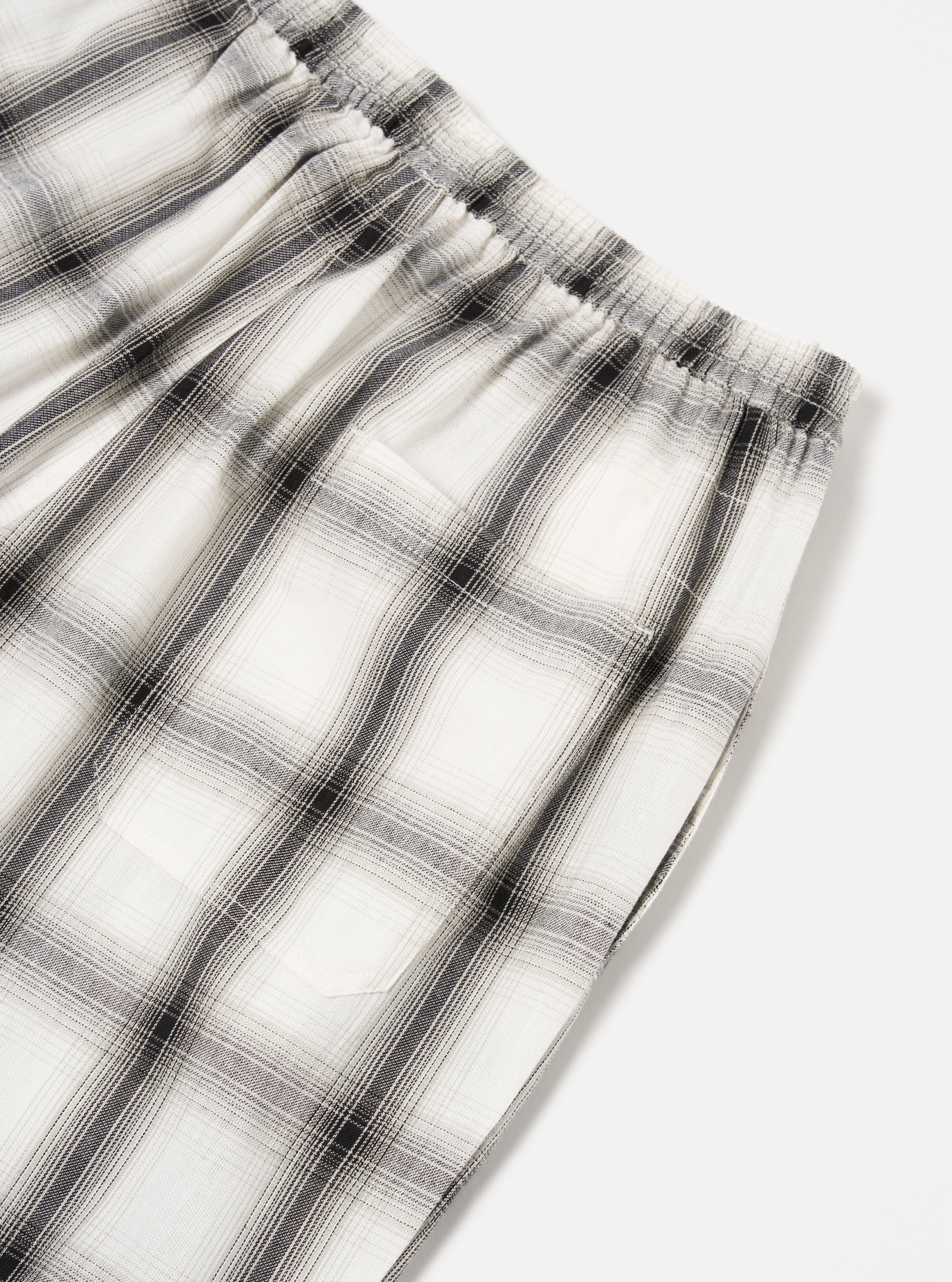 Close-up of the Ecru Shadow Check Pyjama Pant on a white surface. The relaxed fit pant features a shadow check pattern in ecru and grey tones, with an elastic waistband.
