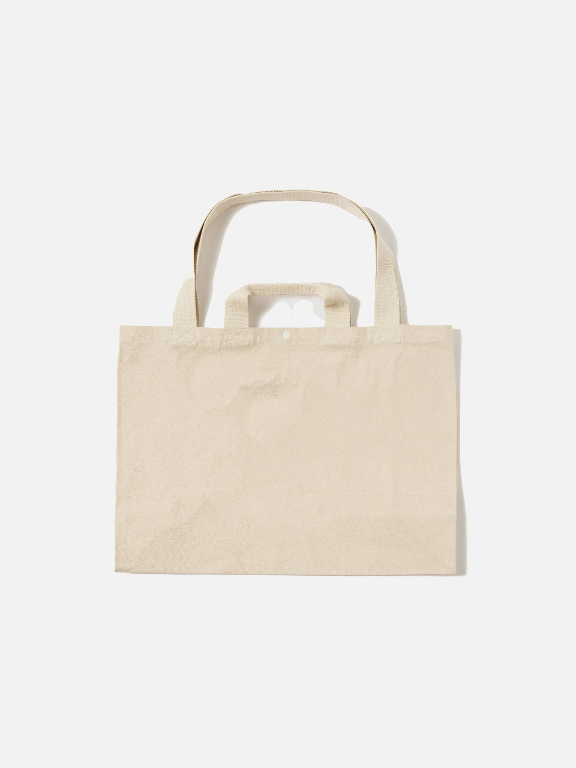 Studio shot of an Ecru Canvas Market Tote on a white background. The tote is a light beige color and made of canvas material. It has two handles and a rectangular shape.