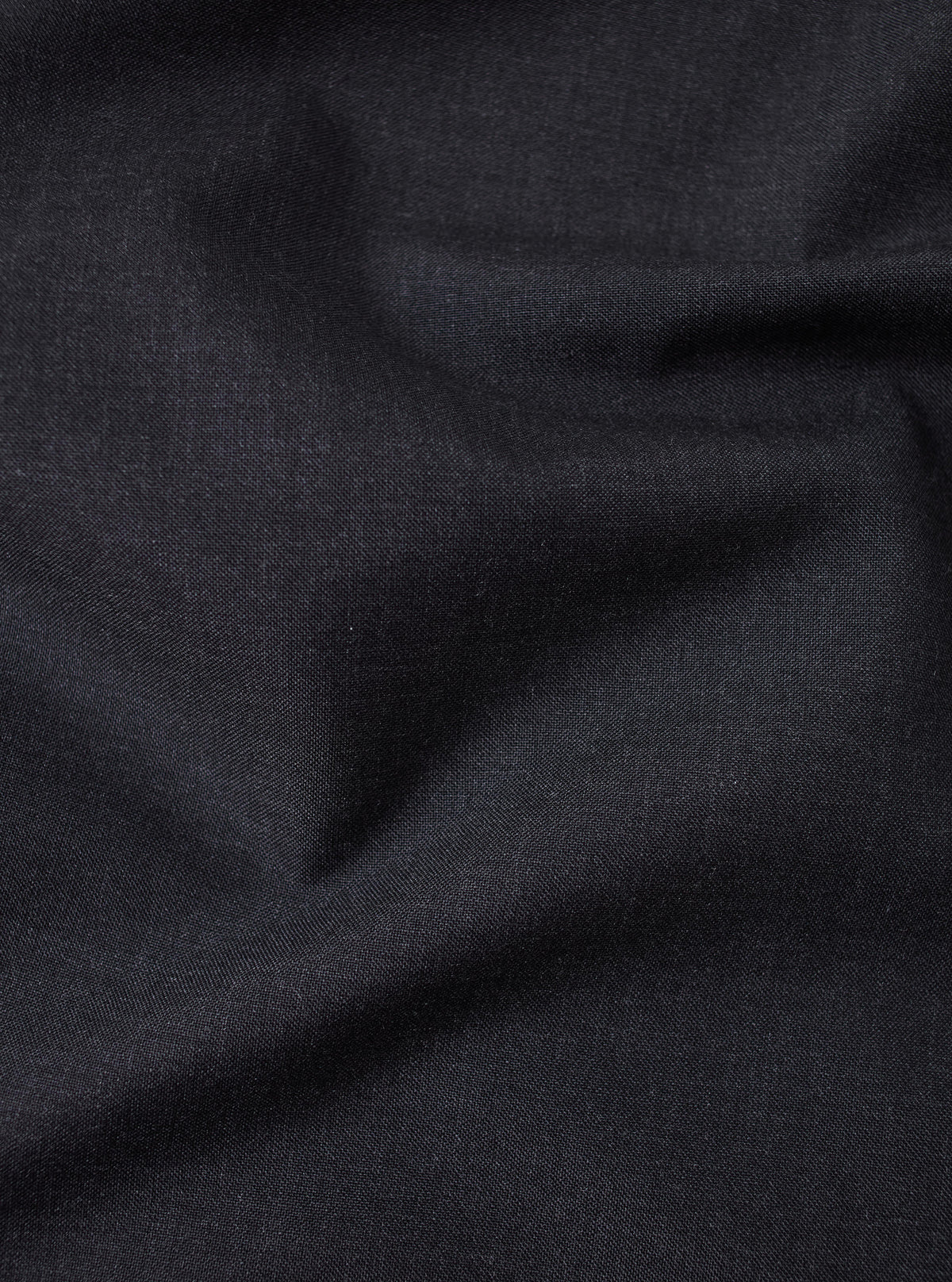 Close-up of the Charcoal Tropical Suiting Oxford Pant fabric. The dark charcoal material is softly draped, showcasing its texture and quality.