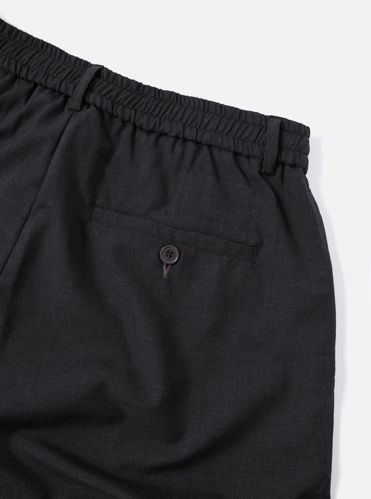 Close-up of the Charcoal Tropical Suiting Oxford Pant, showcasing the elastic waistband, back pocket with button, and the fabric's texture against a clean white background.