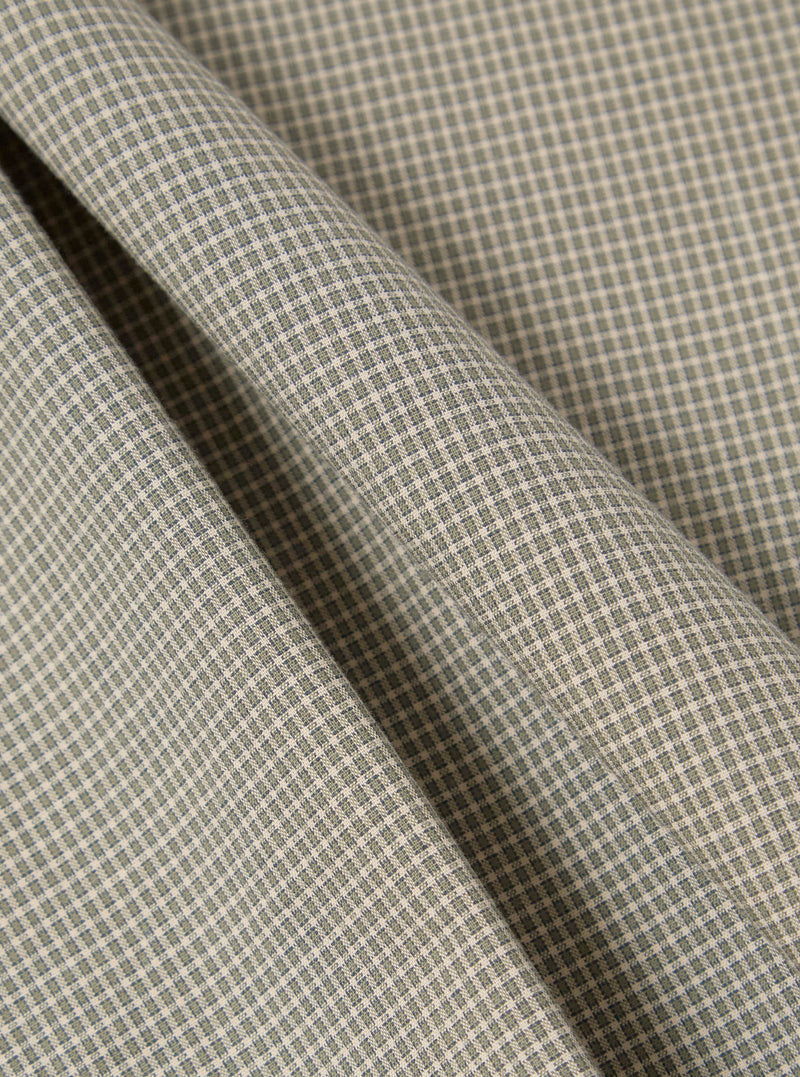 Close-up of the Green Tiny Check Long Pyjama Set fabric. Soft, green and white check pattern. Folded material on a plain surface.