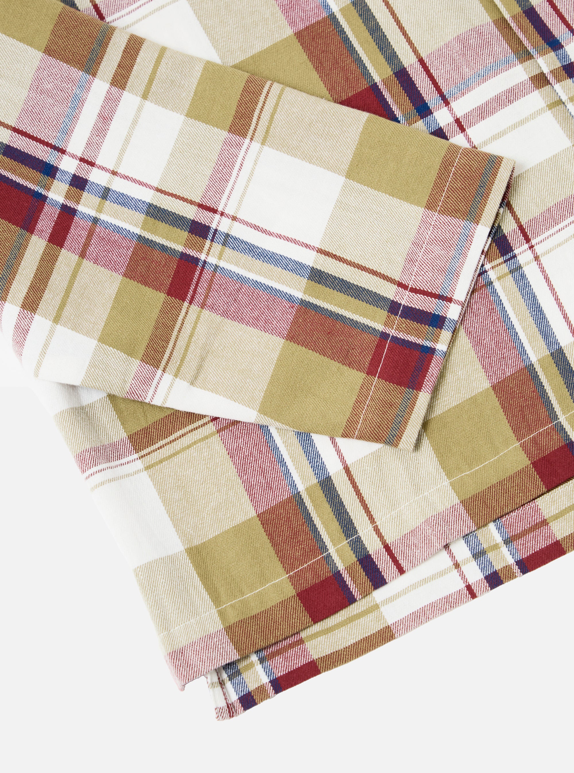 Close-up of the Red/Brown Kip Check Long Pyjama Set fabric. The cotton blend features a red, brown, and blue plaid pattern on a white background. Shot on a white surface.