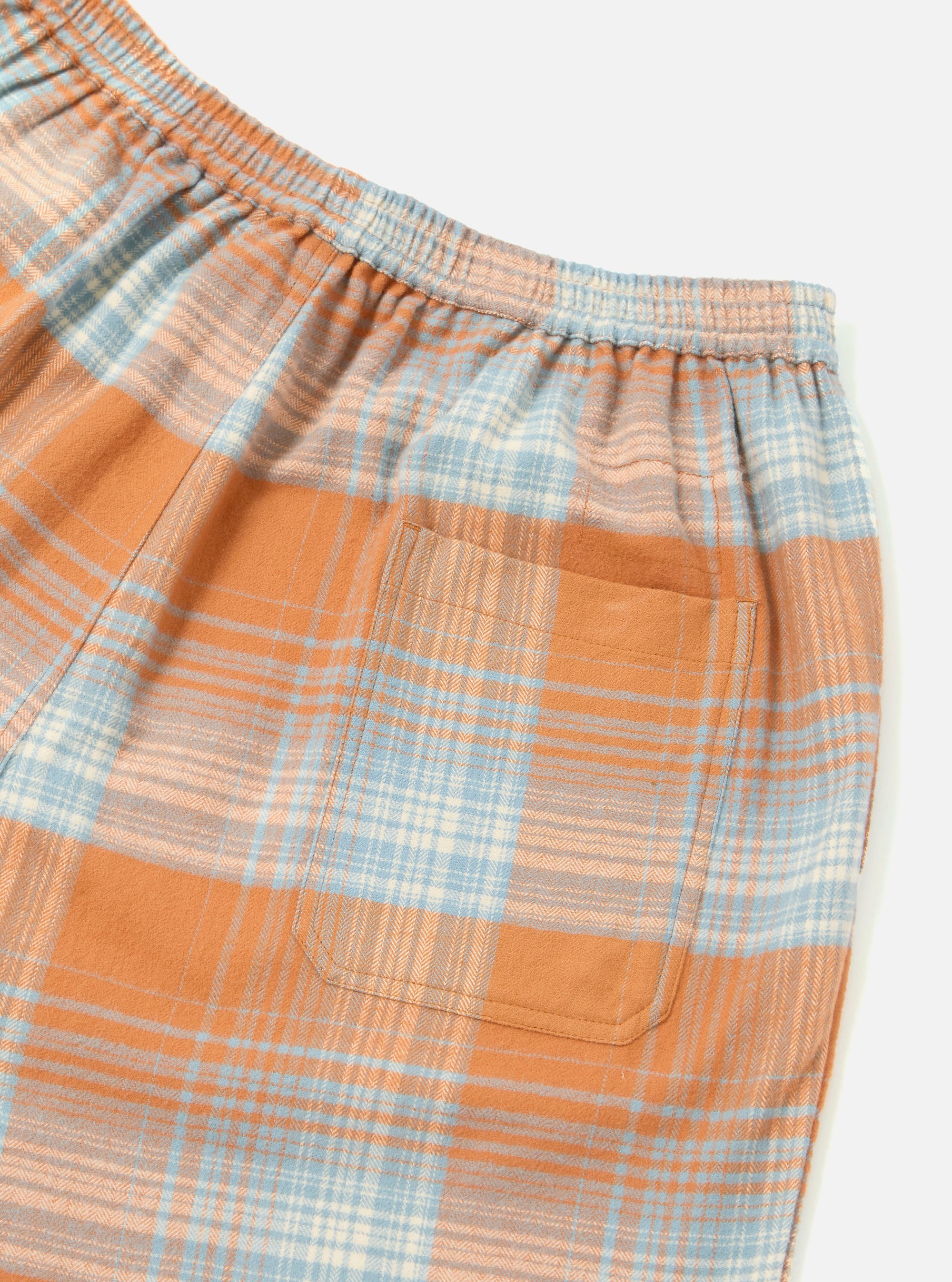 Close-up of the Orange Check Pyjama Short. Features a blue, orange, and white plaid pattern, elastic waistband, and back pocket. Shot on a white background.