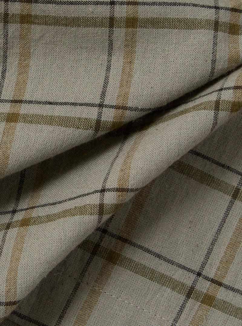 Close-up of the Green PJ Plaid Pyjama Short fabric. The material is a light, neutral tone with green, brown, and black plaid lines. The fabric is folded.