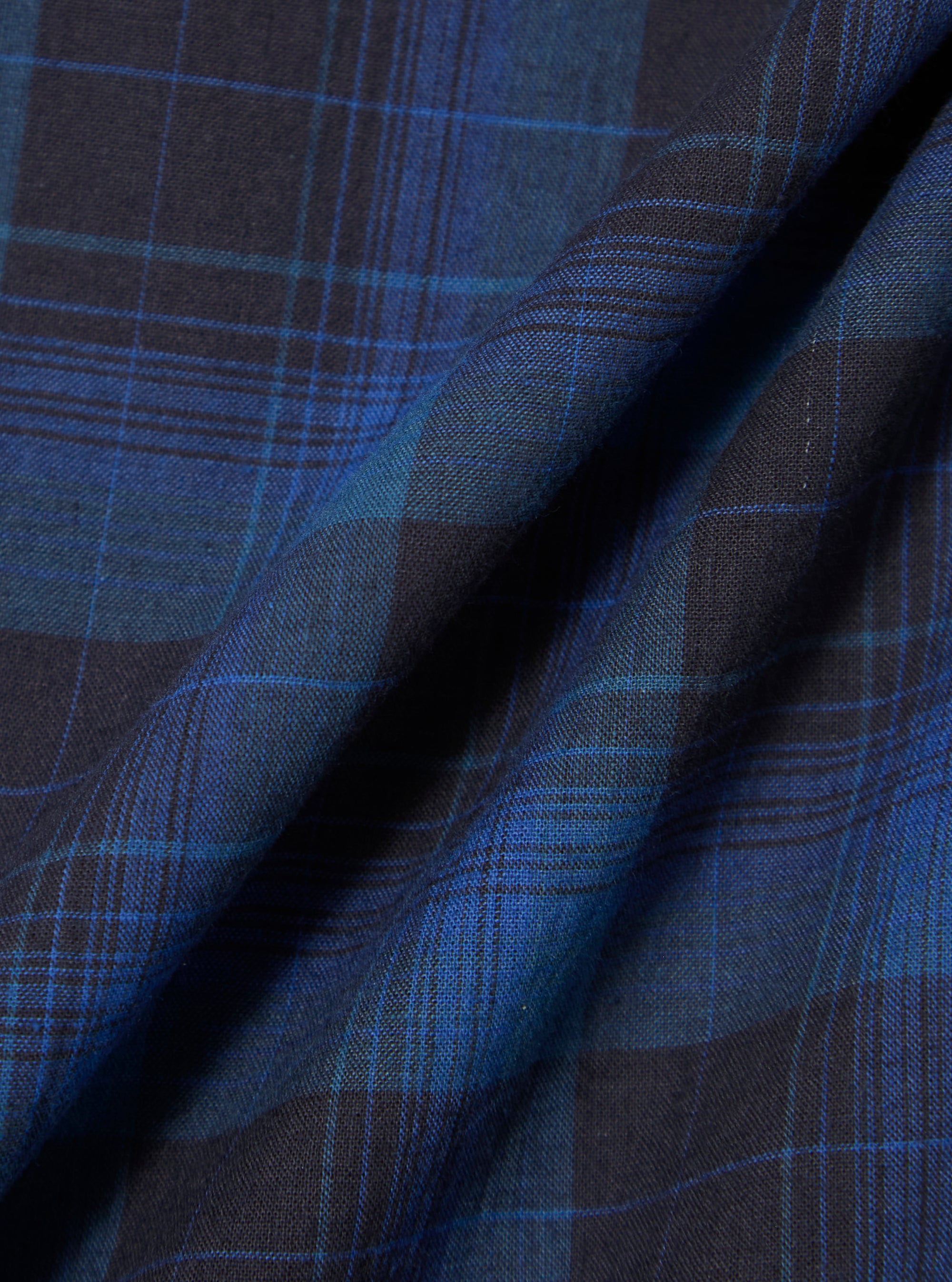 Close-up of the Navy/Blue Check Pyjama Pant fabric. The material is folded, showcasing the navy and blue plaid pattern. The background is a plain surface.