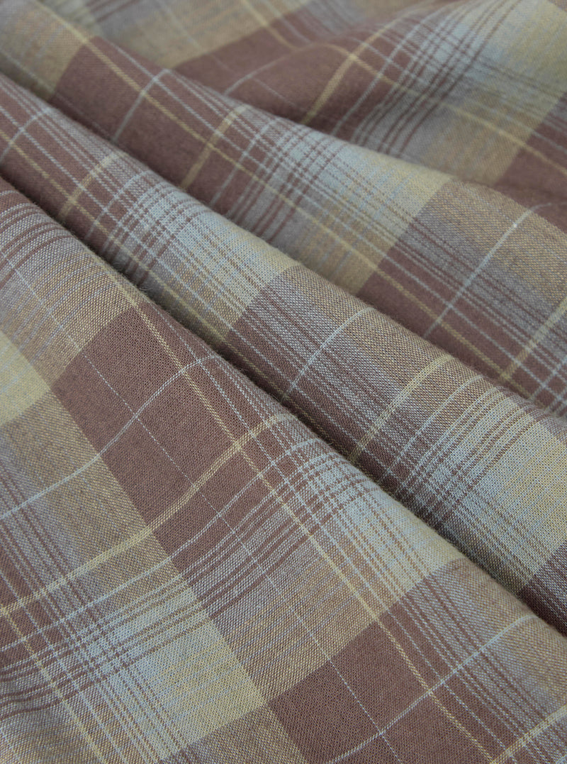 Close-up of the Green/Brown Check Pyjama Pant fabric. The material is folded, showing a detailed plaid pattern in brown, green, and white. The background is a plain surface.