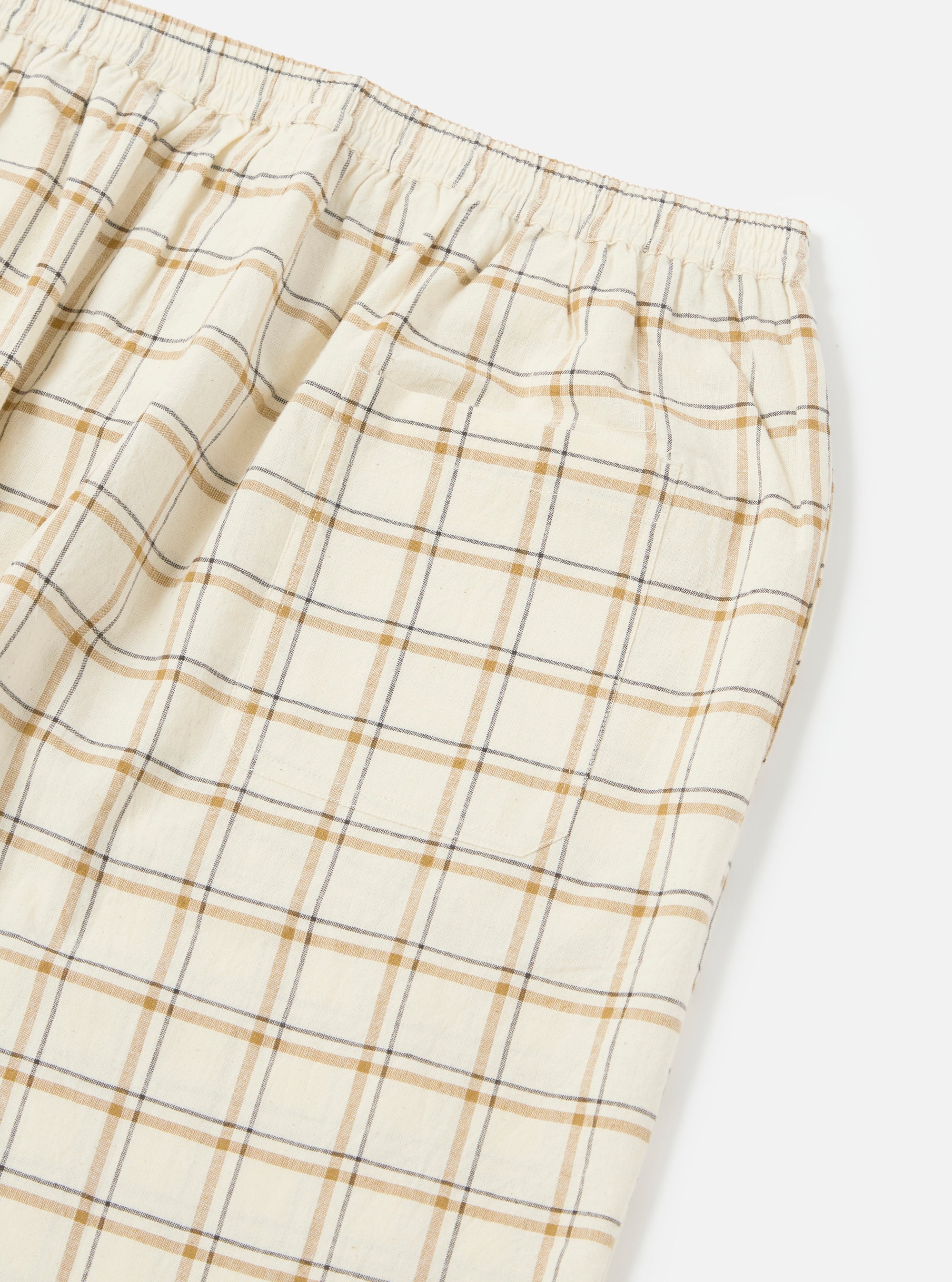 Close-up of the Ecru PJ Plaid Pyjama Pant on a white background. The pants feature an elastic waistband and a plaid pattern in ecru, brown, and black.