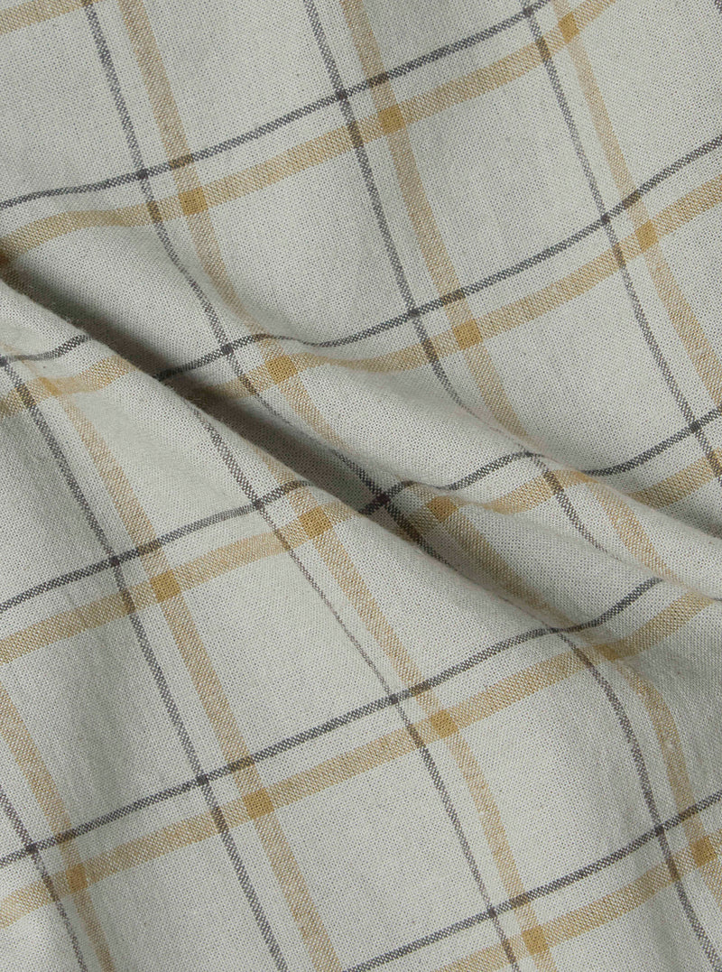 Close-up of the Green PJ Plaid Pyjama Pant fabric. The material is a soft, woven plaid with green, gold, and gray lines on a white background. The fabric is draped on a flat surface.