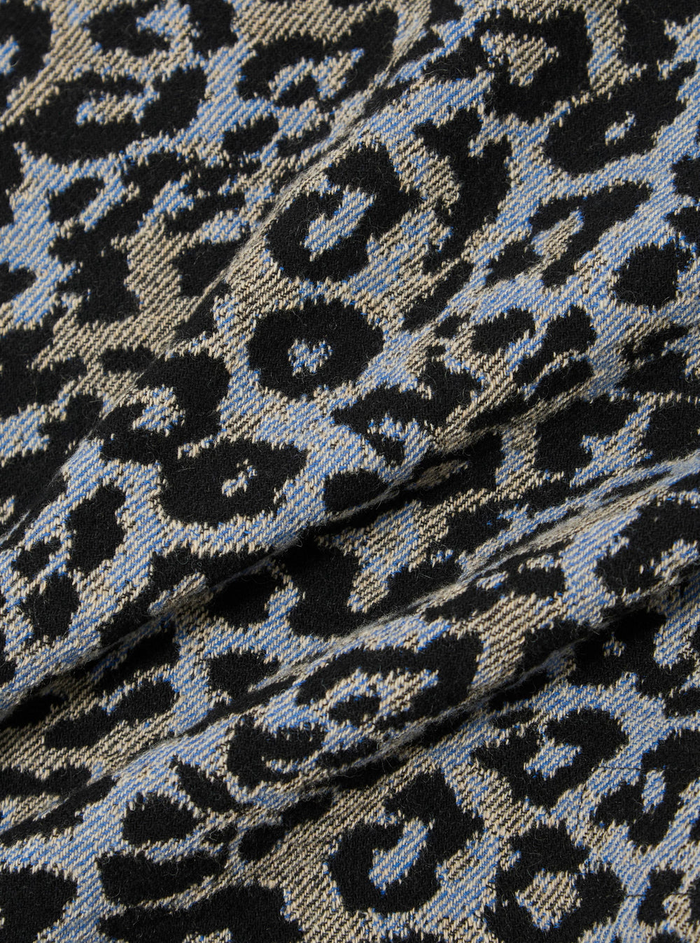 Close-up of the Blue Leopard Flower Wool Club Jacket fabric. The wool has a blue, black, and beige leopard print. The fabric is draped to show texture.