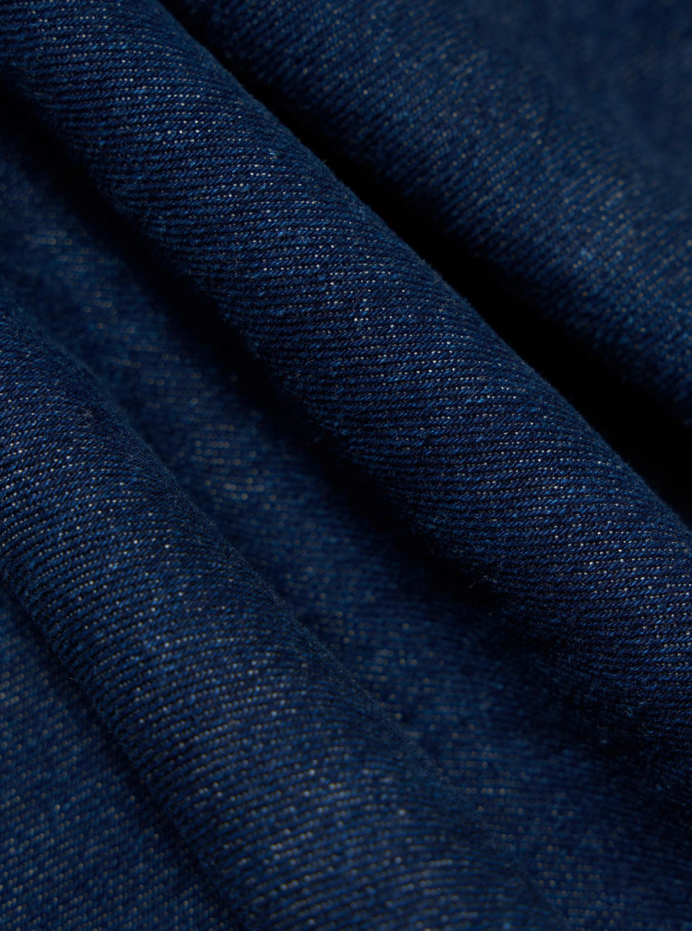 Close-up of the Indigo Work Denim Dutch Pant fabric. The dark blue denim is folded, showing the texture and weave. Studio shot.