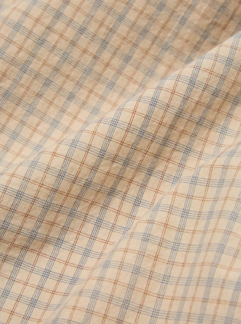 Close-up of the Fawn Shiro Check Lazy Day Shirt fabric. Features a fawn background with blue and brown check pattern. The material is softly draped.