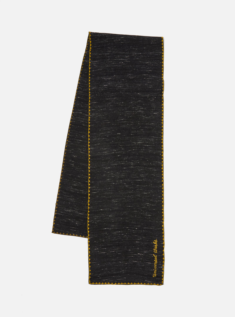 A black wool scarf with yellow trim is displayed on a white background. The Black Wool Scarf has the words 'Universal Works' embroidered on it.