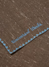 Close-up of a Brown Wool Scarf with blue embroidered trim and logo on a flat surface. The scarf has a subtle speckled pattern.