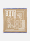 The Sand Single Jersey Neckerchief, a tan cotton square with white geometric and floral prints and a blue border, is laid flat on a white surface.