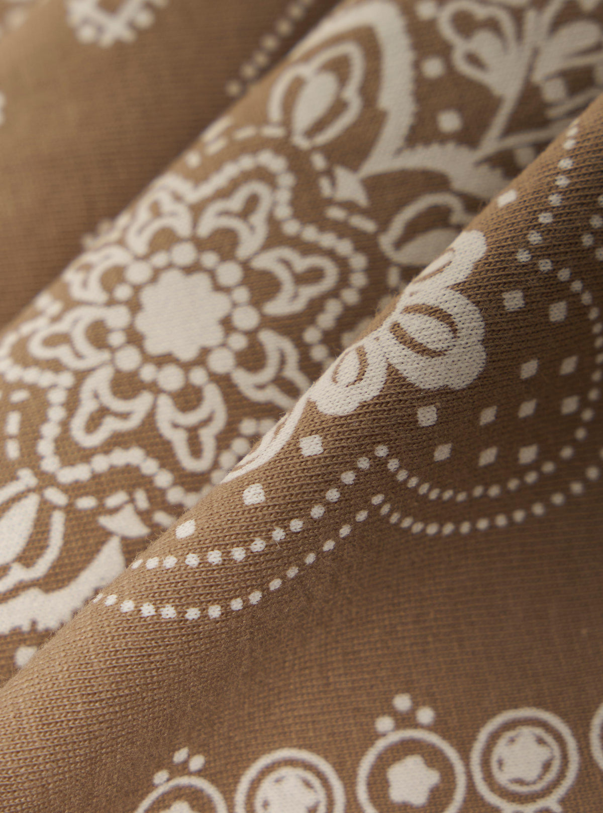 Close-up of the Sand Single Jersey Neckerchief. The fabric is a light brown with a white paisley pattern. The image is cropped to show the texture and design.