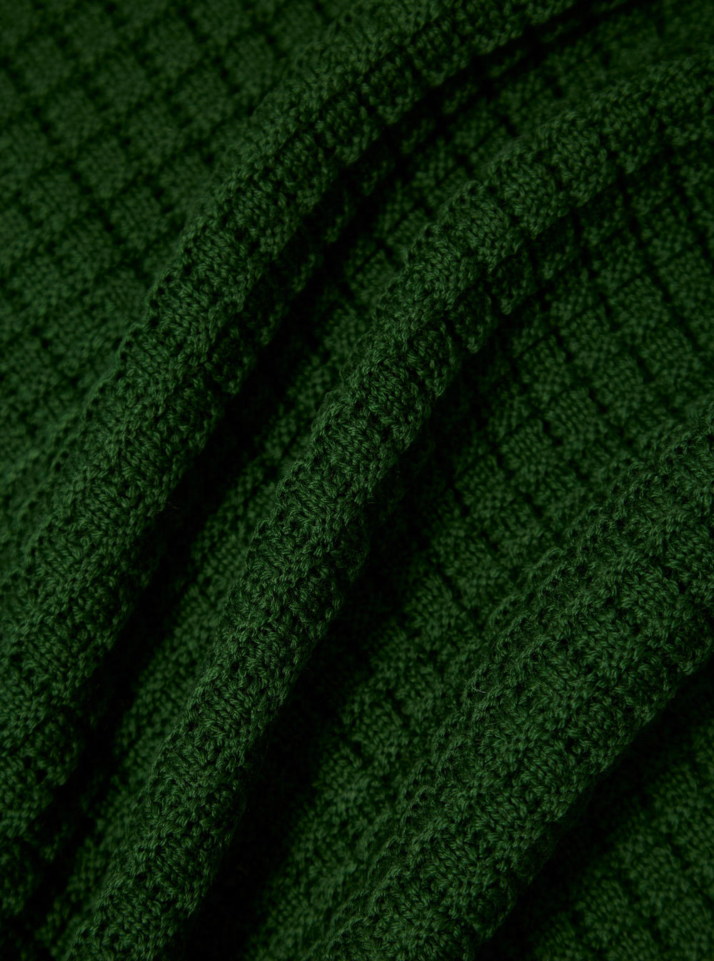 Close-up of the green textured Merino knit Charlie Cardigan, showing the fabric's detail and texture. The background is a simple, dark surface.