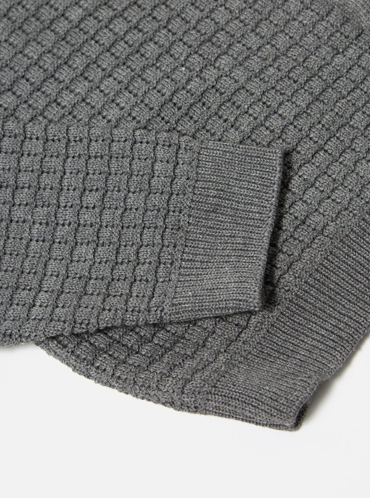 Close-up of the grey textured Merino knit Charlie Cardigan on a white surface, showcasing the intricate knit pattern and soft texture of the cardigan.