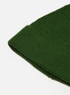 Close-up of a Green Merino Knit Watch Cap on a white surface. The texture of the knit is visible. The cap is folded at the brim.