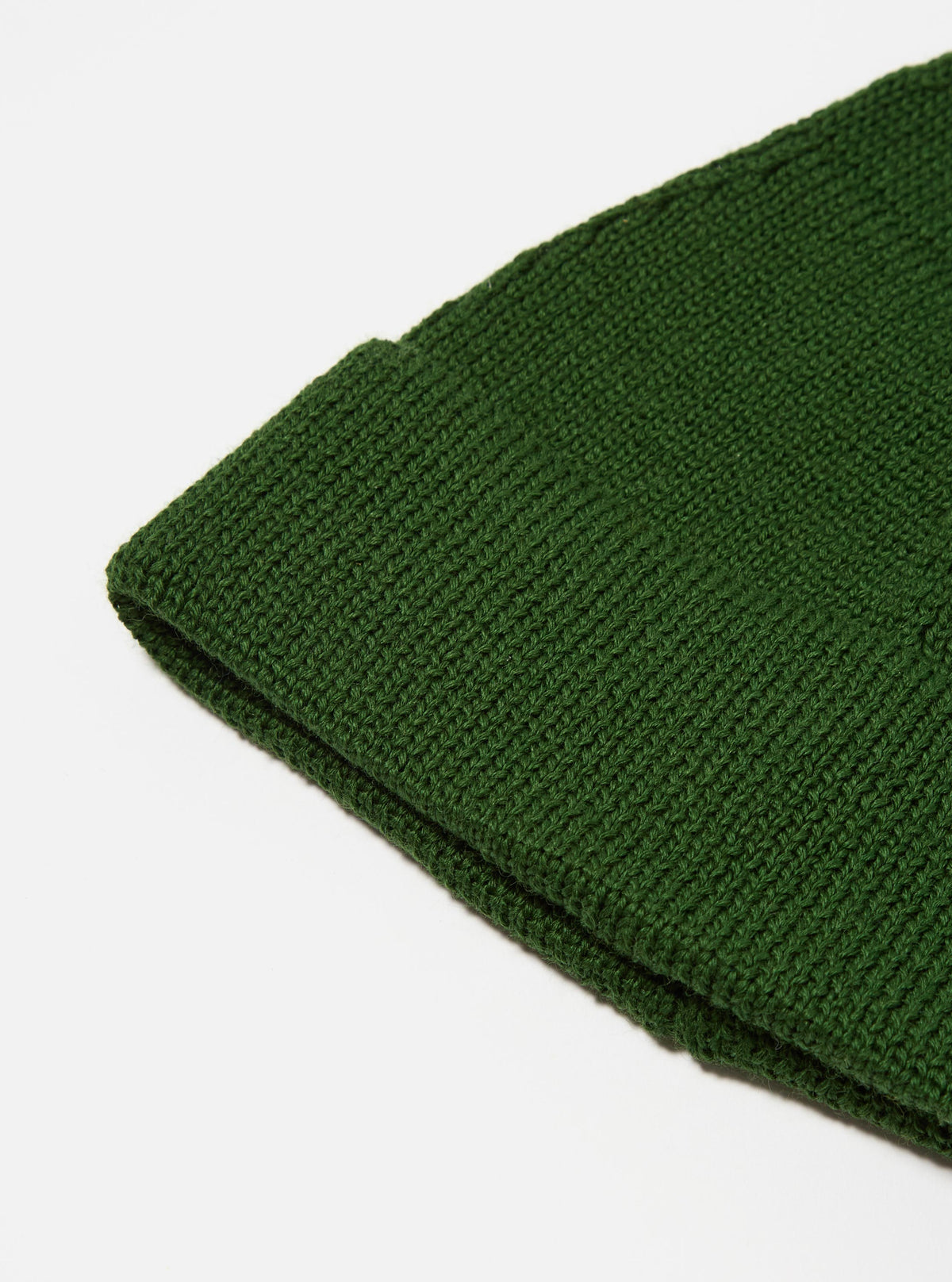 Close-up of a Green Merino Knit Watch Cap on a white surface. The texture of the knit is visible. The cap is folded at the brim.