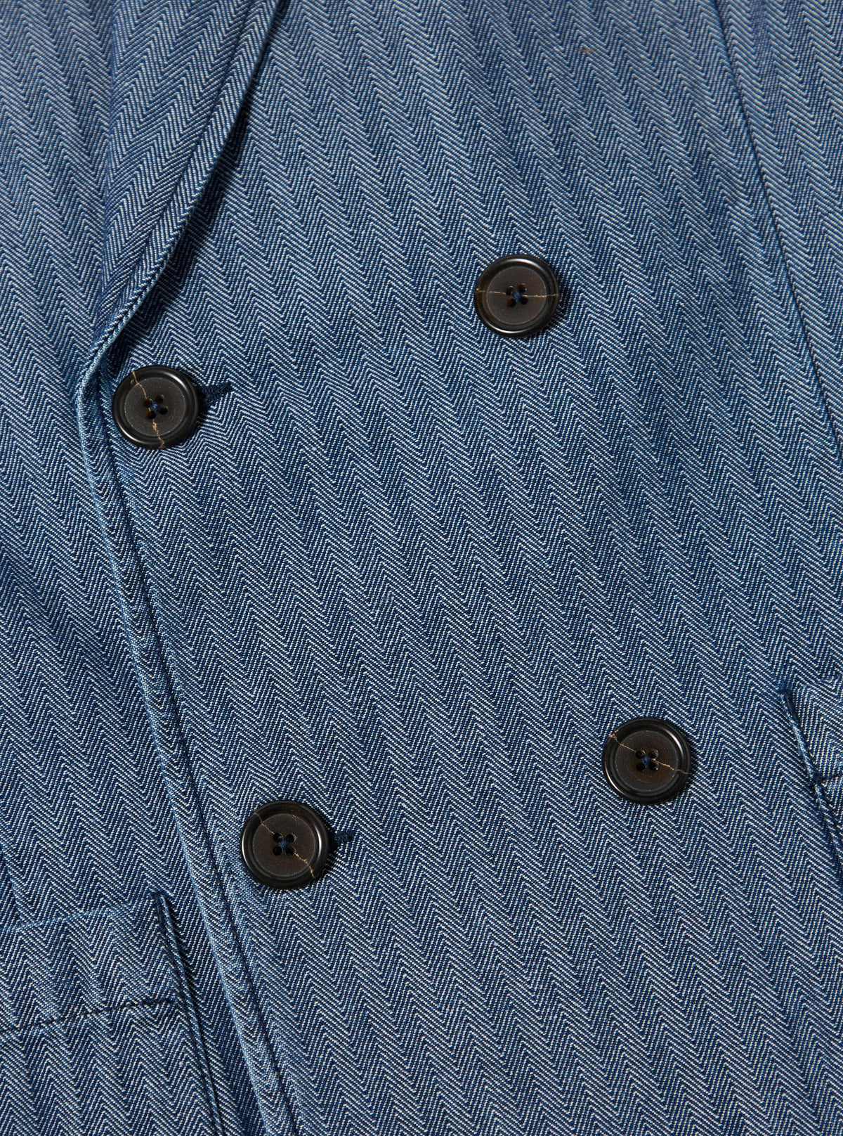 Close-up of the Indigo Denim Herringbone Manor Jacket, showcasing the blue herringbone pattern, dark buttons, and tailored fit. The image highlights the jacket's texture and design details.