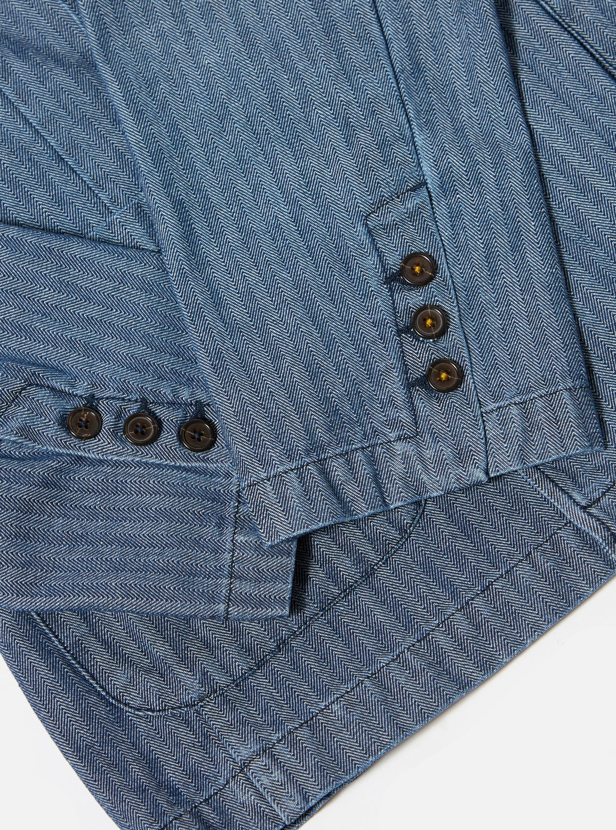 Close-up of the Indigo Denim Herringbone Manor Jacket showing the blue herringbone pattern, brown buttons, and tailored fit on a white background.