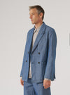 A man poses in profile against a white backdrop, wearing an Indigo Denim Herringbone Manor Jacket. The jacket is a double-breasted style with a subtle herringbone pattern.