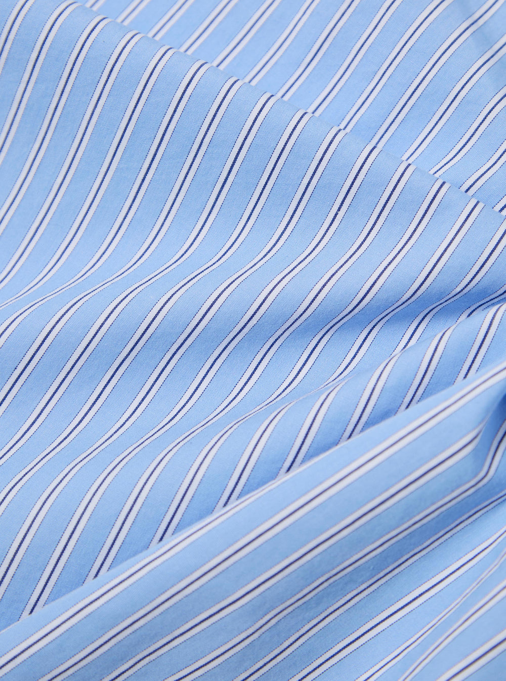 Close-up of the Blue Vila Stripe Wide Lazy Day Shirt. Features a light blue fabric with thin navy and white stripes. The shirt is folded on a white surface.