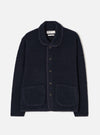 A male model stands against a plain neutral studio background wearing the Navy Alvar Fleece Lancaster Jacket. The front-view image displays the deep navy blue shade, cozy shawl collar, front button closure, and two patch pockets.