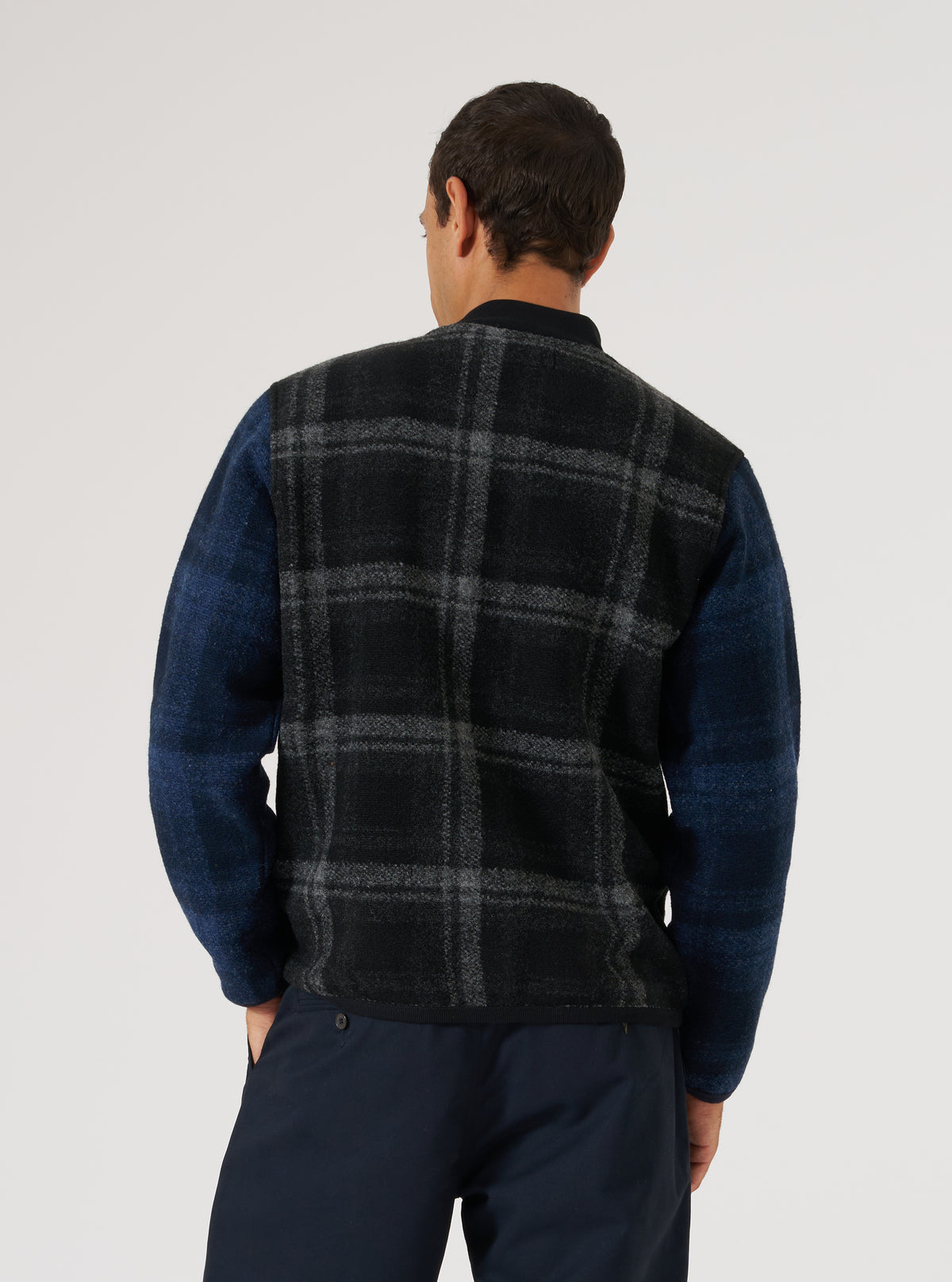Back view of a man wearing the Grey Moh Check Fleece Button Front Bomber. The bomber has a grey and black check pattern on the body and blue sleeves. Shot against a white backdrop.
