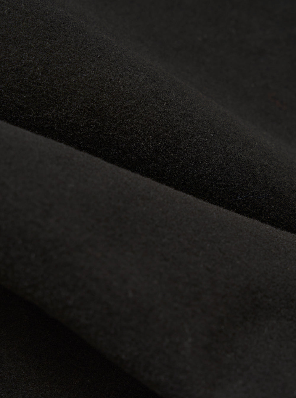 Close-up of the Black Comfort Moleskin Field Jacket fabric. The dark, soft material is draped to show texture. Studio shot on a neutral background.