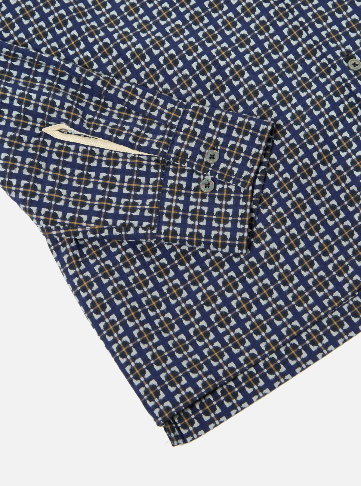 Close-up of the Navy Oscar Cotton L/S Camp Shirt on a white surface. Shows the shirt's navy cotton fabric with a geometric pattern in white, black, and gold. The shirt has a pocket and buttoned cuff.
