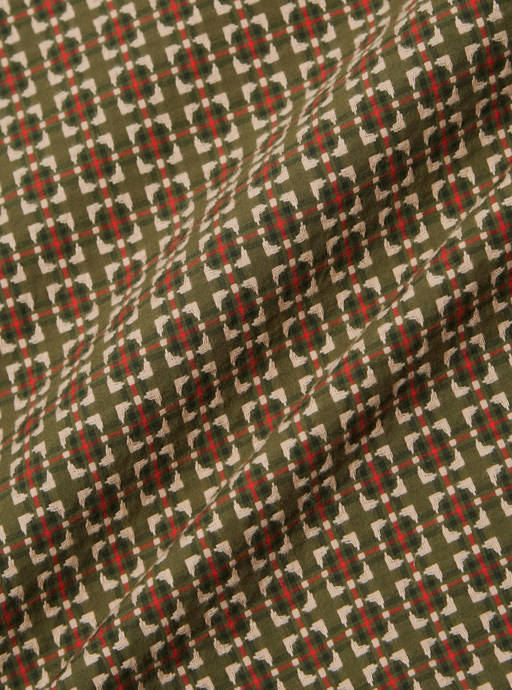 Close-up of the Olive Oscar Cotton L/S Camp Shirt fabric. Features an olive green base with a red and white geometric pattern. The shirt is laid on a flat surface.