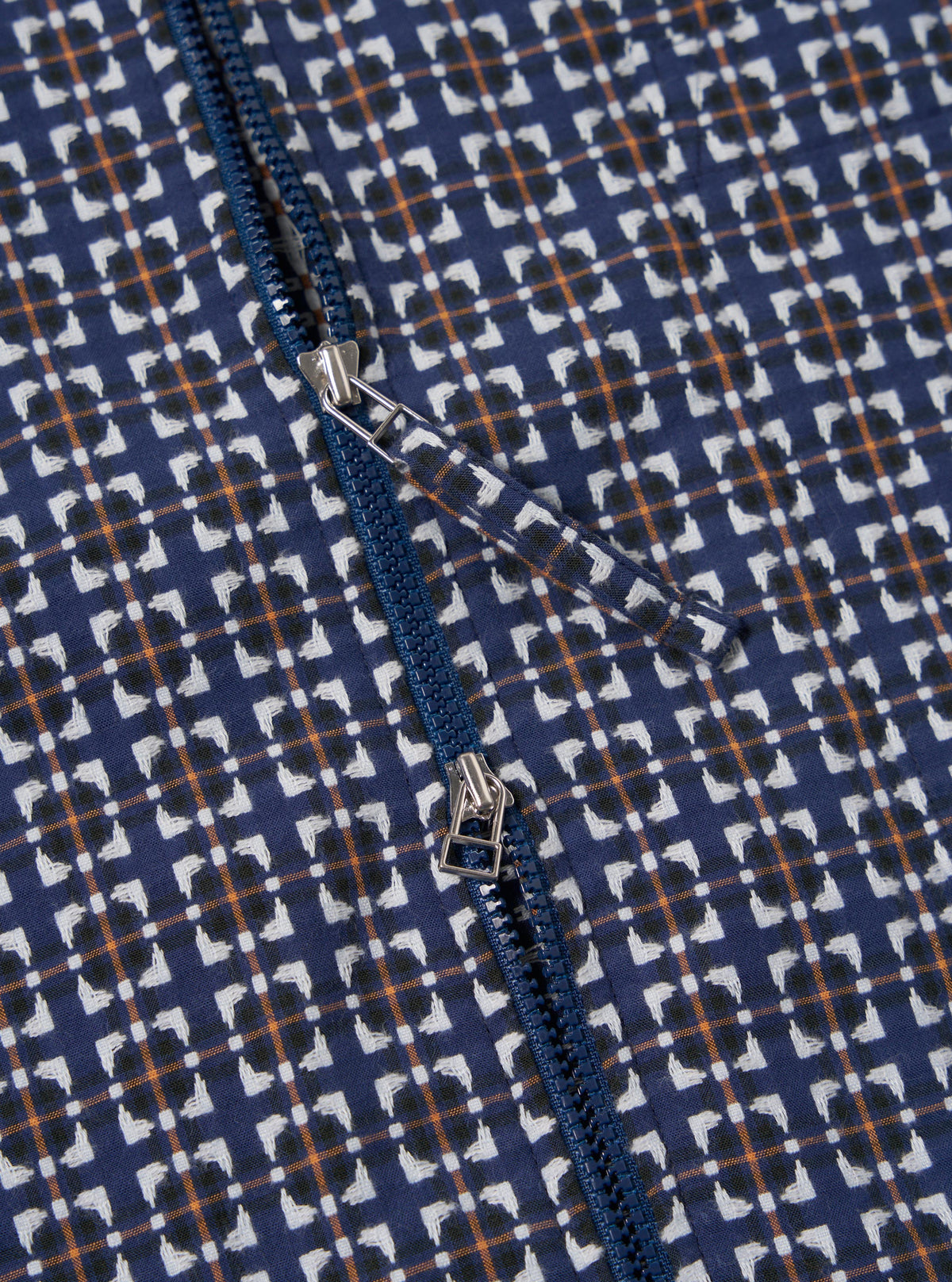 Close-up of the Navy Oscar Cotton Zip Shirt, showcasing its navy, white, and orange pattern and blue zipper. The shirt is laid flat on a neutral surface.