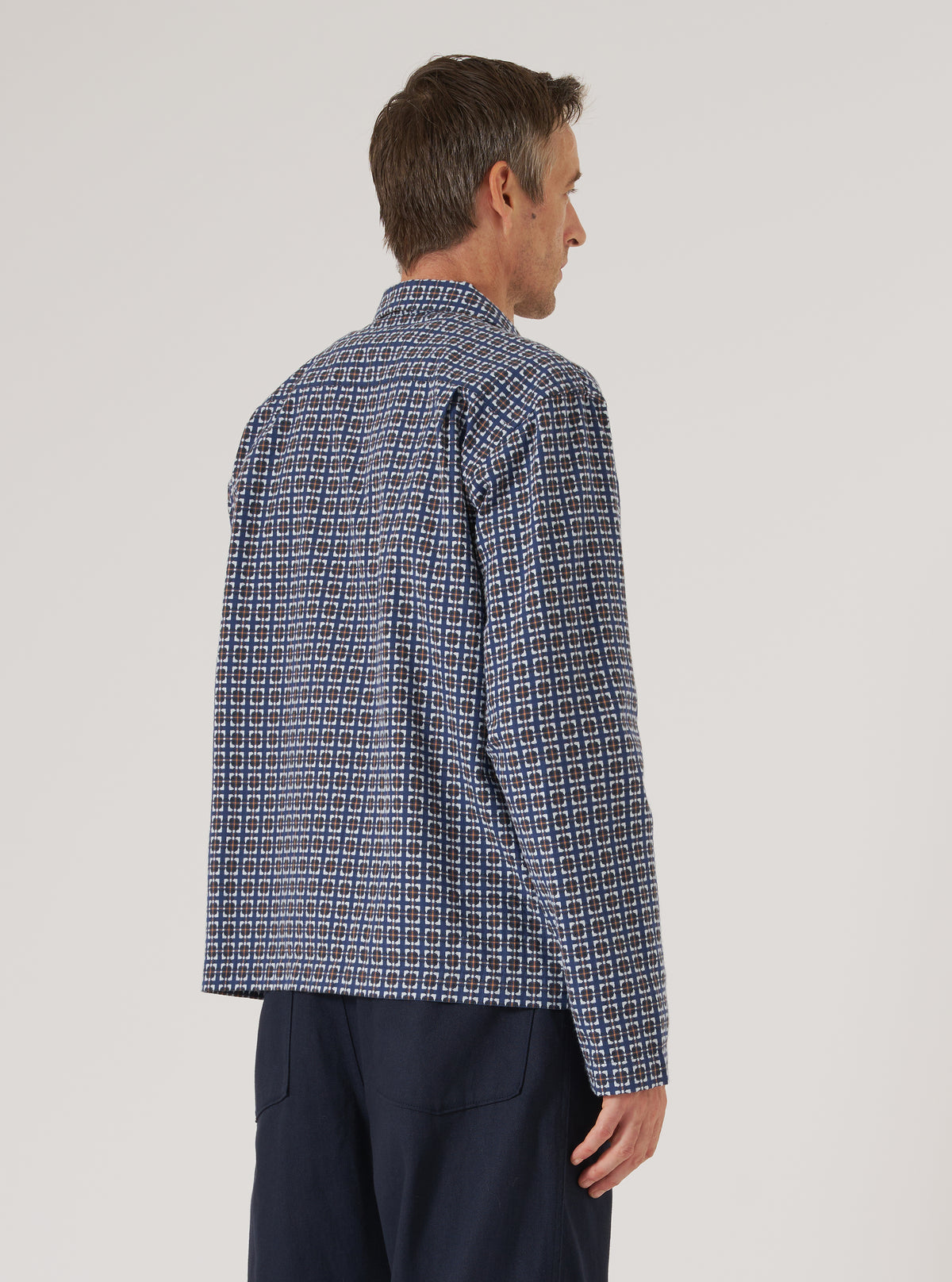 A man stands against a white backdrop, modeling the Navy Oscar Cotton Zip Shirt. The shirt features a geometric pattern. The model is also wearing navy trousers.